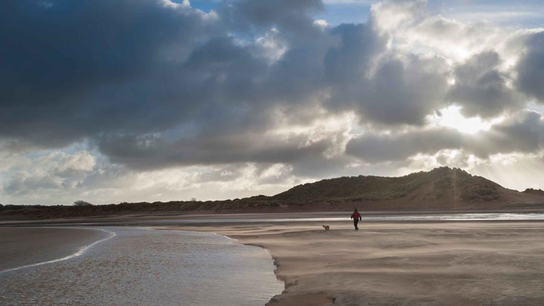 Visitor walking dog on the beach at Sandscale Haws National Nature Reserve, Lake District